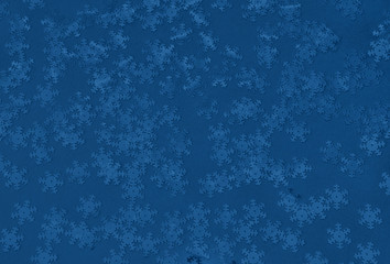 Metallic foil snowflakes confetti sparse on trendy classic blue colored background. Simple holiday concept. Winter festive backdrop. Top view, flat lay. Color of the year 2020.