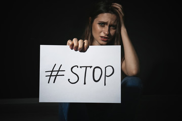 Crying young woman with hashtag STOP on black background. Domestic violence concept