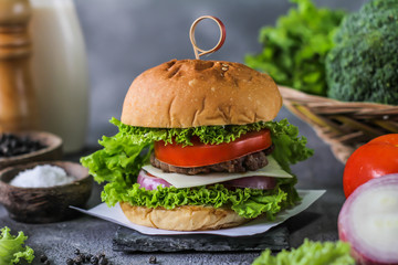 Photo of fresh burger on wooden cutting board on dark background..Homemade hamburger with beef, onion, tomato, lettuce and cheese. Homemade fast food. Dark textured background. Copy space. Image.