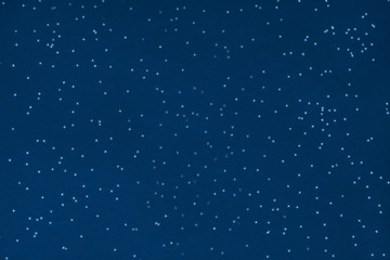 Metallic foil stars confetti sparse on trendy blue colored background. Simple holiday concept. Winter festive backdrop. Top view, flat lay. Color trend concept.