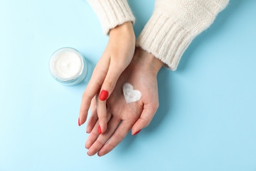 Woman hands, moisturizing cream for clean and soft skin in winter time, jar of cream, sweater, heart shape created from cream on blue background, space for text. Top view. Healthcare concept