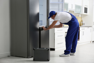 Male technician with screwdriver repairing refrigerator in kitchen