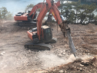 Fototapeta premium Hydrohammer is crushing rocks during road construction works on the rocky soils. Heavy machinery at earthmoving