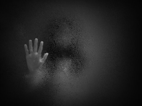 Horror scary shadow of woman behind  glass in black and white. Blurred of  ghost or dead people in darkness. Stressed girl trapped in the room, concept of Halloween or violence against children.