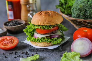 Photo of fresh burger on wooden cutting board on dark background..Homemade hamburger with beef, onion, tomato, lettuce and cheese. Homemade fast food. Dark textured background. Copy space. Image.
