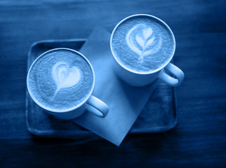 Two cup of cappuccino art on a wooden table colored classic blue