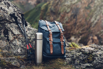Fototapeta Hipster Blue Backpack, Thermos And Trekking Poles Closeup, Front View. Tourist Traveler Bag On Rocks Background. Adventure Hiking Tourism Outdoor Concept obraz
