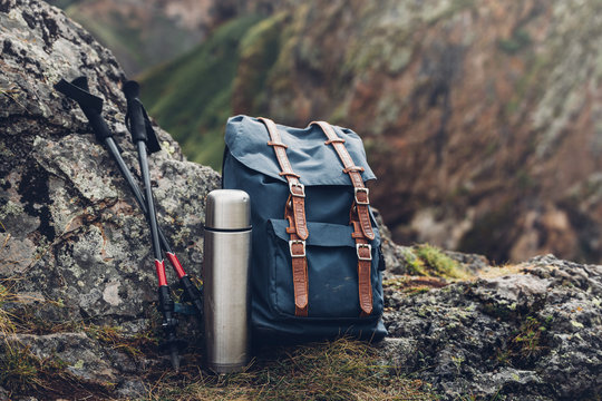 Hipster Blue Backpack, Thermos And Trekking Poles Closeup, Front View. Tourist Traveler Bag On Rocks Background. Adventure Hiking Tourism Outdoor Concept