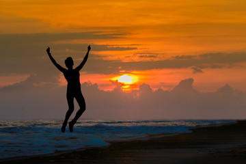 Fototapeta premium Happy sport woman silhouette jumping for joy on the beach at big sunset. Success, winner, happiness