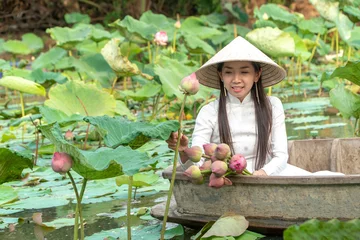 Foto op Canvas Beautiful asia women wearing white traditional Vietnam dress (Ao Wai) and Vietnam farmer's hat and sitting on wooden boat in flower lotus lake. Her hands picking lotus flowers. © Prot