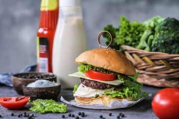 Photo of fresh burger on wooden cutting board on dark background..Homemade hamburger with beef, onion, tomato, lettuce and cheese. Homemade fast food. Dark textured background. Copy space. Image.