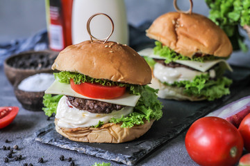 Photo of fresh burger on wooden cutting board on dark background..Homemade hamburger with beef, onion, tomato, lettuce and cheese. Homemade fast food. Dark textured background. Copy space. Image.