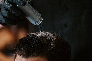 cropped view of barber holding bottle with white powder above head of man in barbershop
