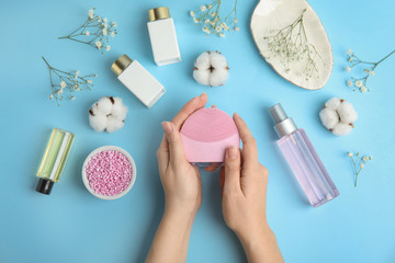 Woman with face cleansing brush on light blue background, top view. Cosmetic accessory