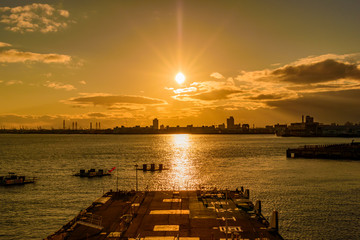 オレンジ色の夕日を反射する海面が見える港の風景
