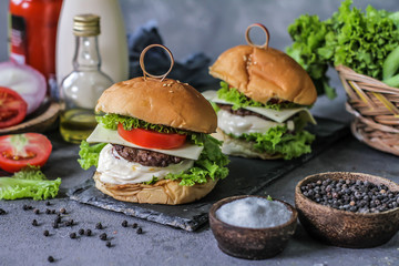 Photo of fresh burger on wooden cutting board on dark background..Homemade hamburger with beef, onion, tomato, lettuce and cheese. Homemade fast food. Dark textured background. Copy space. Image.