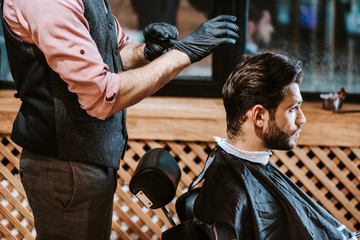 barber wearing black latex gloves near man in barbershop