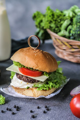 Photo of fresh burger on wooden cutting board on dark background..Homemade hamburger with beef, onion, tomato, lettuce and cheese. Homemade fast food. Dark textured background. Copy space. Image.