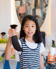 Teenage girl donating her healthy hair to cancer patients. Asian kid holding and showing her...