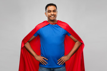 super power and people concept - happy smiling indian man in red superhero cape with arms on hips...