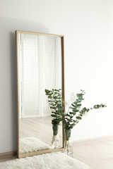 Large mirror with wooden frame near white wall in light room