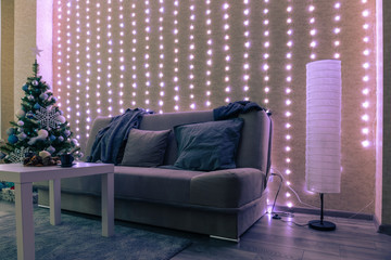 interior of a dark cozy room with a sofa, Christmas tree and garlands on the wall