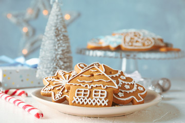 Plate with Christmas cookies, Christmas trees, toys, gift boxes on white table, against blue background, closeup