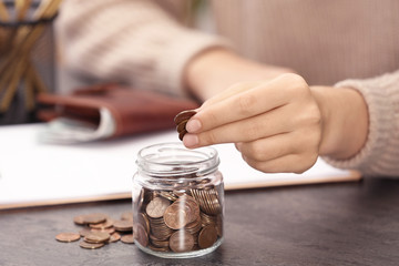 Woman putting money into glass jar at table, closeup