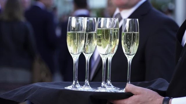 Waiter offer a glass of champagne on a tray. Fine classy champagne is served during a ceremony. Slowmotion