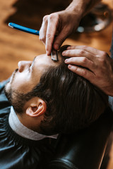 Fototapeta premium selective focus of barber holding sharp razor while doing haircut to man