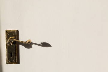 A door handle on a white door in the sun.