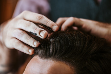 Fototapeta premium cropped view of barber with black hair pomade on hands styling hair of man