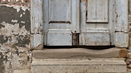 Stone steps worn out by many feet, weathered wooden entrance door and flaky exterior wall