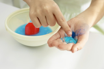Little girl adding colored sparkles to homemade slime toy at table, closeup