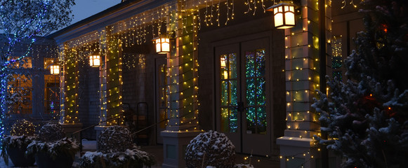 A house festively decorated with New Year and Christmas garlands and toys on a snowy winter evening. USA. Maine