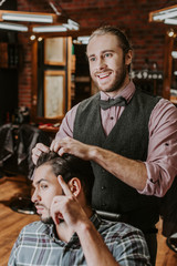 cheerful barber styling hair on handsome bearded man