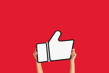 Hands holding the sign of like on red studio background. Negative space to insert your text or...