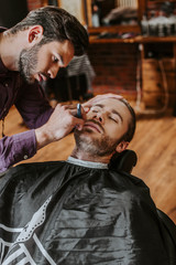 handsome barber holding razor while shaving man