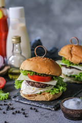 Photo of fresh burger on wooden cutting board on dark background..Homemade hamburger with beef, onion, tomato, lettuce and cheese. Homemade fast food. Dark textured background. Copy space. Image.
