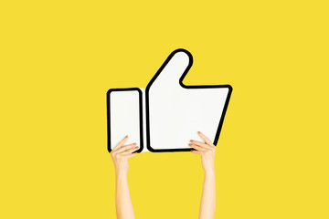 Hands holding the sign of like on yellow studio background. Negative space to insert your text or...