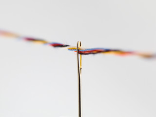 multiple colorful threads passing through the eye of a needle
