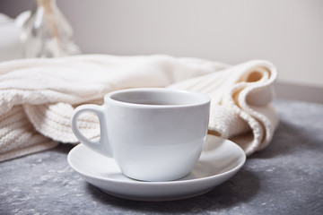 Close up of cup of coffee and knittead white plaid on the gray background