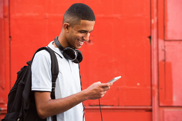 Close up side of smiling young arabic man looking at mobile phone by red background