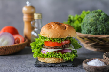 Photo of fresh burger on wooden cutting board on dark background..Homemade hamburger with beef, onion, tomato, lettuce and cheese. Homemade fast food. Dark textured background. Copy space. Image.