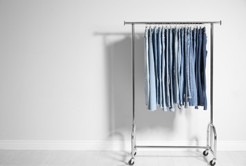Rack with different jeans near light wall. Space for text
