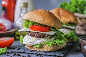 Photo of fresh burger on wooden cutting board on dark background..Homemade hamburger with beef, onion, tomato, lettuce and cheese. Homemade fast food. Dark textured background. Copy space. Image.