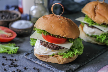 Photo of fresh burger on wooden cutting board on dark background..Homemade hamburger with beef, onion, tomato, lettuce and cheese. Homemade fast food. Dark textured background. Copy space. Image.