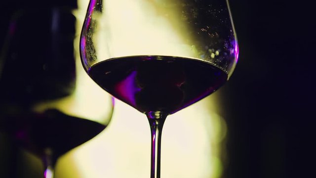 Close up slow motion shot, wine glass with party lights in background inside club. Party, event, celebration concept.
