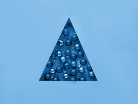 Geometric creative Christmas flat lay. Monochrome image toned in blue color. Xmas baubles in triangular paper hole in triangular shape of Christmas tree.