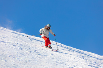 Fototapeta na wymiar Girl On the Ski. a skier in a bright suit and outfit with long pigtails on her head rides on the track with swirls of fresh snow. Active winter holidays, skiing downhill in sunny day. Dynamic picture